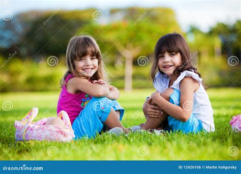 Dos Muchachas Sonrientes Jovenes Que Se Sientan En La Hierba Foto De