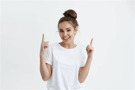 positive european woman pointing up with both index fingers while smiling cheerfully at camera