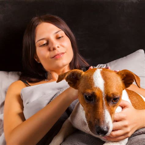 Young Beautiful Brunette Woman Plays In Bed With Her Dog Stock Image