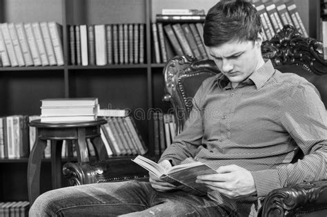 Serious Young Man Sitting On A Chair Reading Book Stock Photo Image