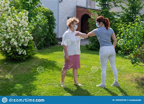 Two Masked Women Greet Their Elbows In The Park An Elderly Woman And Her Daughter Maintain