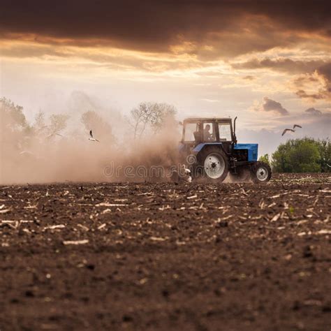 Tractor Plows A Field In The Spring Against A Beautiful Sunset Sky