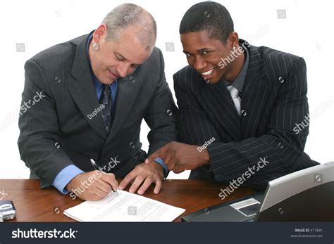 Two Men In Suits At Desk Signing Papers Shot In Studio Over White