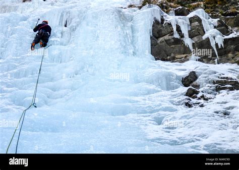 Male Mountain Guide Lead Ice Climbing A Frozen Waterfall In Deep Winter