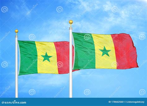 Senegal And Senegal Two Flags On Flagpoles And Blue Cloudy Sky Stock