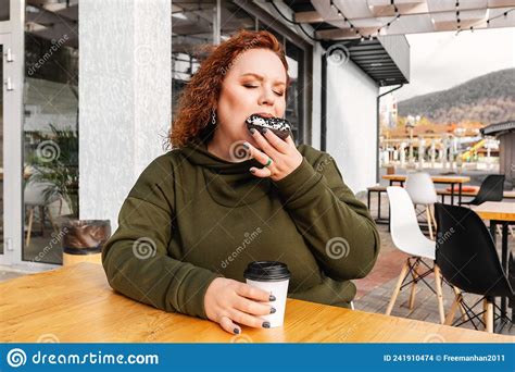 Portrait Of Overweight Enjoing Woman Eating A Chocolate Donut At Cafe