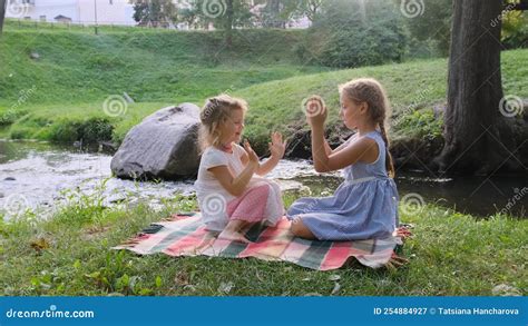 two teenage girls play with each other clapping their hands while sitting on the riverbank the