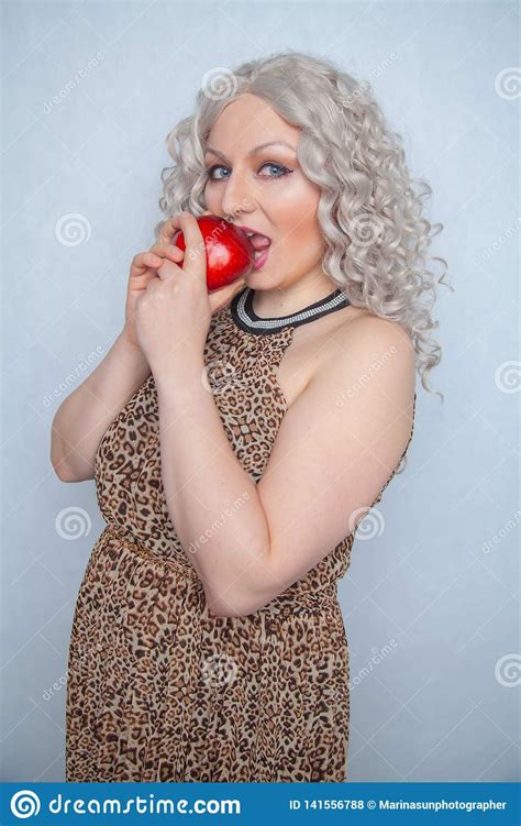 chubby blonde girl wearing summer dress and posing with big red apple on white background alone
