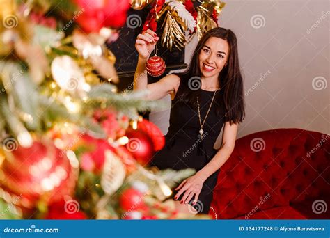 Smiling Brunette Decorates A Christmas Tree Brunette Woman Holding A Christmas Ball In Her Hand