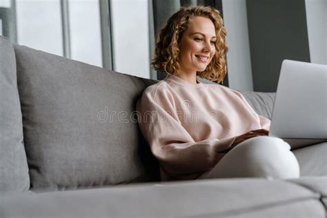 white blonde woman smiling and using laptop while sitting on couch stock image image of couch