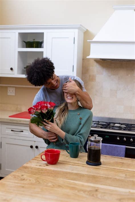 Biracial Young Man Holding T And Closing Happy Wife S Eyes With Hand At Table In Kitchen