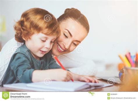 Madre Sonriente Que Enseña A Su Hijo A Escribir Imagen De Archivo
