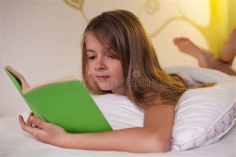 Young Girl Lying On Her Belly In Bed Reading A Book Shallow D Stock