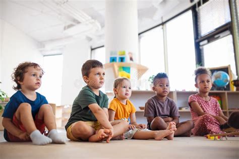 Grupo De Crianças Pequenas Da Escola Primária Sentados No Chão Em Sala De Aula Levantando Mãos