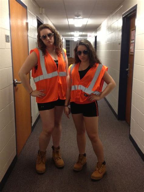 Two Women In Orange Vests And Black Shorts Standing Next To Each Other On A Hallway