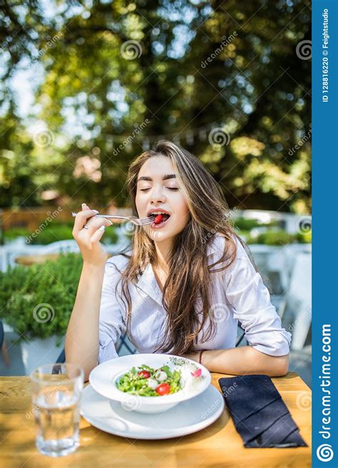 Smiling Young Woman Enjoys Fresh Vegetable Salad At Cafe Has Lunch