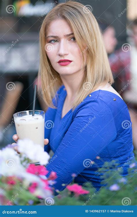 Charming Caucasian Blonde Girl In A Blue Dress Sitting At A Table In A
