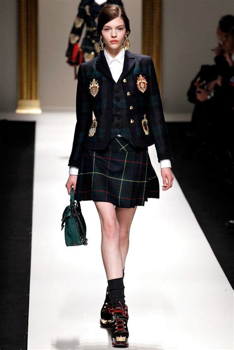 A Woman Walking Down A Runway Wearing A Skirt And Jacket With Patches