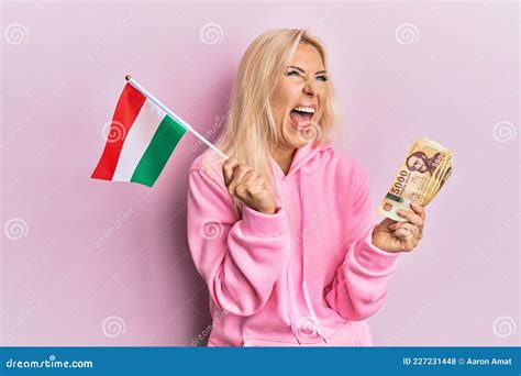 Young Blonde Woman Holding Hungary Flag And Forint Banknotes Angry And Mad Screaming Frustrated