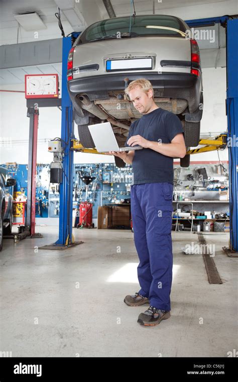 Full Length Portrait Of Young Mechanic Using Laptop In His Auto Repair