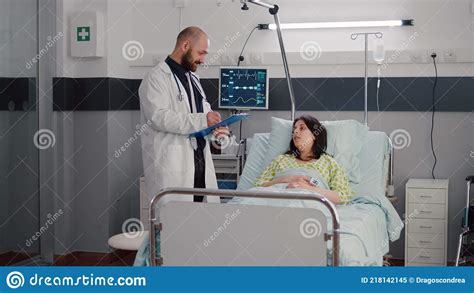 Assistant With Dark Skin Helping Patient To Sit Comfortable In Hospital