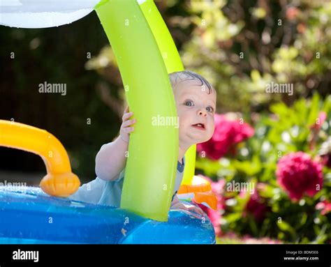 A Baby Boy Playing In An Inflated Plastic Boat Paddling Pool On A