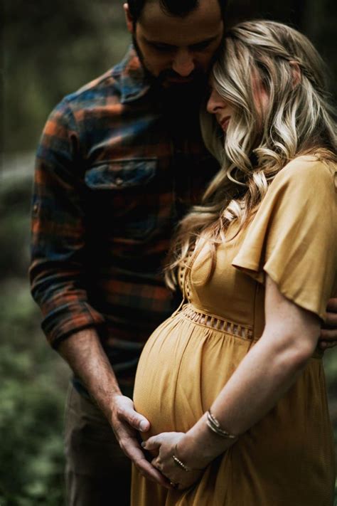A Pregnant Couple Cuddles In The Woods While Holding Each Other S Belly