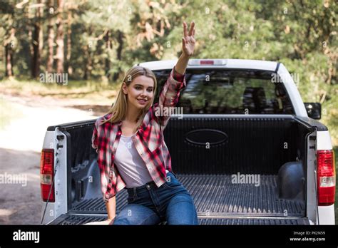 Happy Blonde Girl Waving And Sitting On Pickup Truck In Forest Stock Photo Alamy
