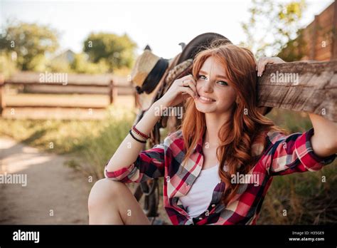 Cheerful Cute Redhead Cowgirl Sitting And Resting At The Ranch Fence
