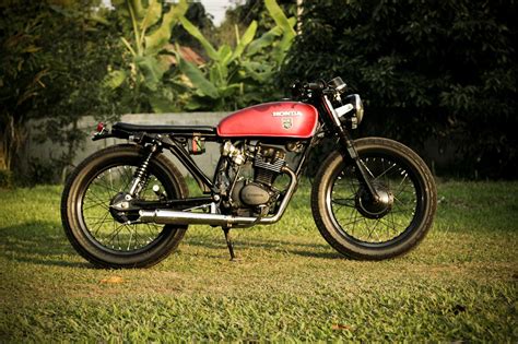 A Red And Black Motorcycle Parked On Top Of A Lush Green Field Next To