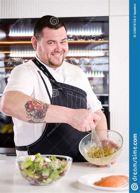 40 Years Man Chef Cooker In A White Uniform And A Black Apron In The Kitchen Of The Restaurant