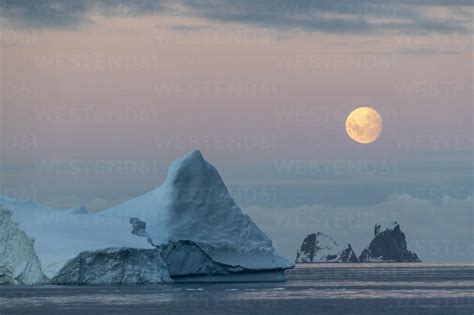 Nearly Full Moon Setting Over Small Islands And Icebergs Off The