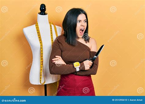 Young Brunette Woman Standing By Manikin Holding Scissors Angry And Mad