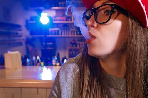 Premium Photo Young Pretty Woman In Red Cap Smoke An Electronic Cigarette At The Vape Shop Closeup