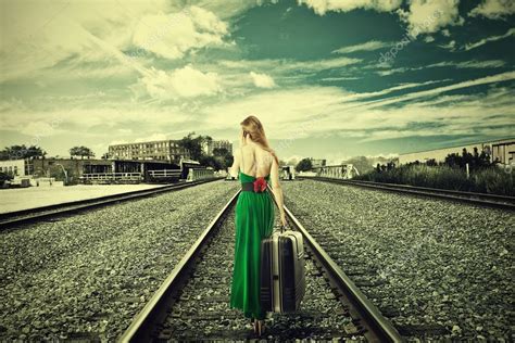 mujer joven con maleta alejándose en las vías del tren hablando por teléfono 2023