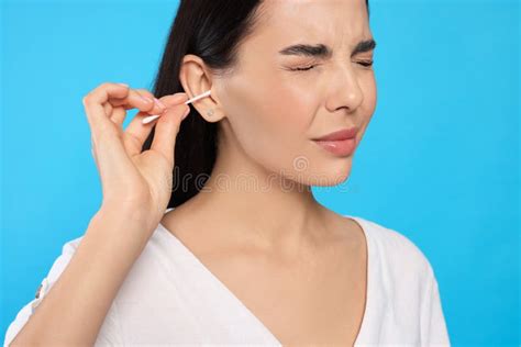 Young Woman Cleaning Ear With Cotton Swab On Light Blue Background