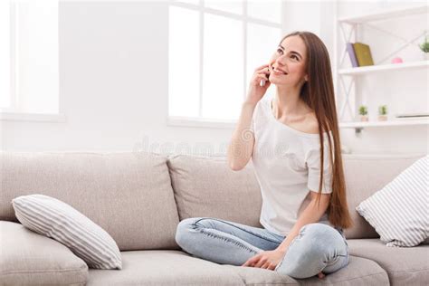 Young Woman Sitting On Sofa And Talking On Cell Phone Stock Photo
