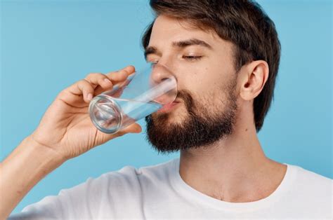 Premium Photo Beautiful Man Drinking Water From A Glass On A Blue Background Close Up Portrait