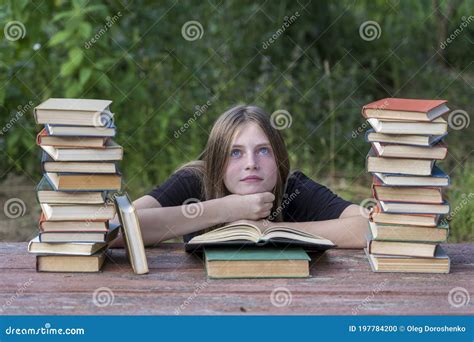 Jeune Fille Lisant Un Livre Et Des Rêves Dans Le Jardin à Une Table En Bois Avec Une Pile De