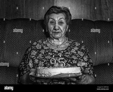 a grayscale shot of a 95 year old woman holding her birthday cake while sitting on the couch