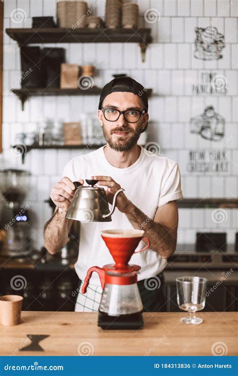 Young Barista In Eyeglasses And Cap Standing At Bar Counter And