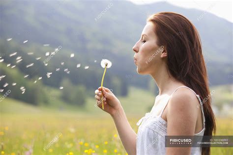 Young Woman Blowing Dandelion In Field Of Flowers — Close Up Side View