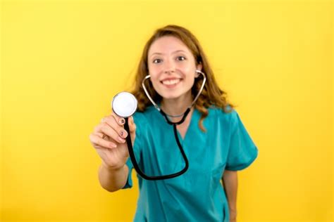 free photo front view of female doctor using stethoscope on a yellow wall