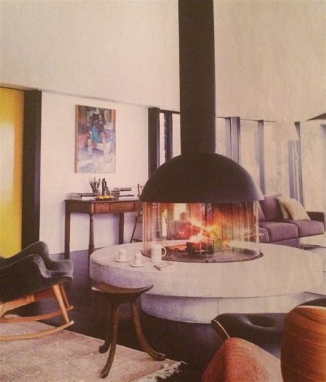 A Living Room With A Fire Place In The Middle Of It And Chairs Around It