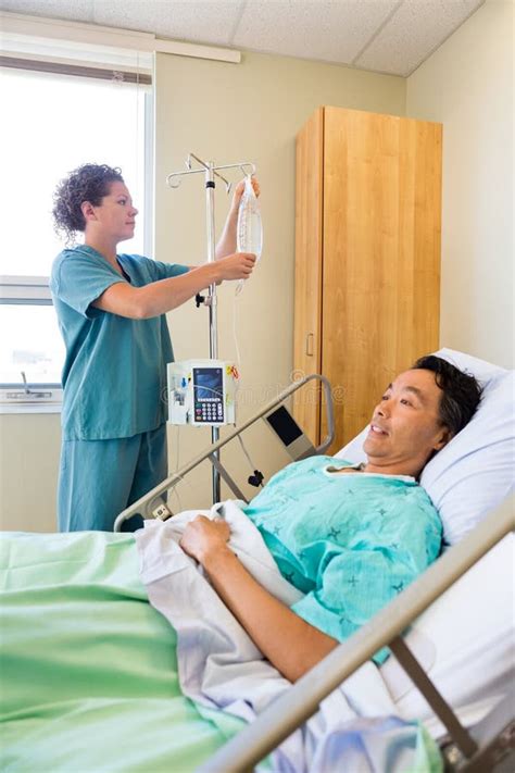 Медсестра регулируя потек IV на штанге с пациентом дальше Стоковое Фото изображение