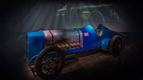 An Old Blue Race Car On Display In A Dark Room With Light Coming From