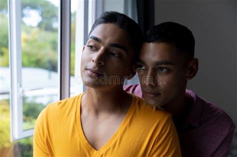 diverse gay male couple looking through a window and embracing stock image image of together