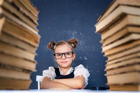 Happy Smart Girl In Rounded Glasses Sitting Between Two Piles Of Books