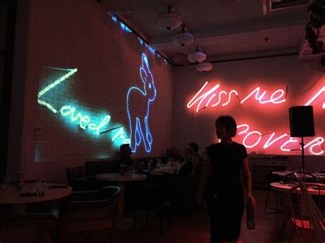 A Person Standing In Front Of A Wall With Neon Signs On It And People