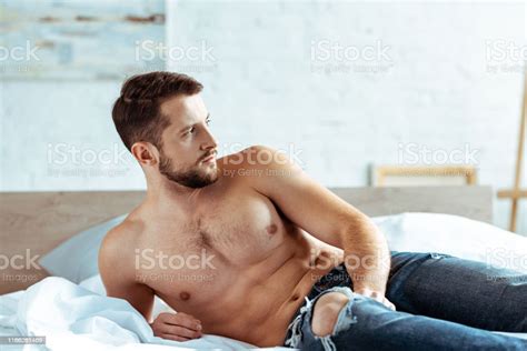 Handsome And Muscular Man Lying On Bed And Looking Away In Bedroom